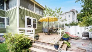 Une maison verte dotée d’une terrasse en bois, de mobilier d’extérieur et d’une pergola avec un parasol.