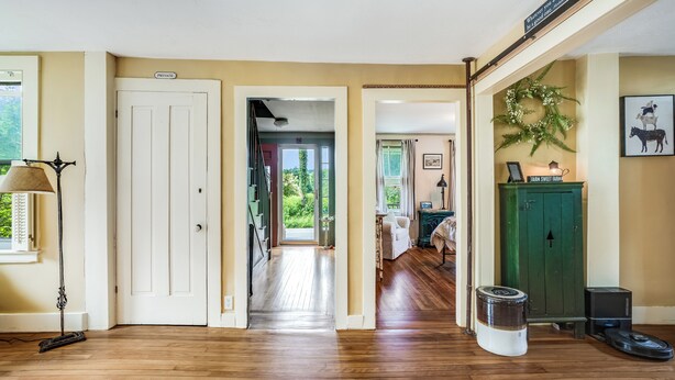 Un vaste couloir doté d’un plancher en bois, une porte blanche portant l’inscription « PRIVÉ », et une vue sur une pièce où l’on aperçoit un meuble vert et un tableau encadré accroché au mur.