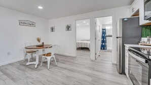 Eine moderne Küche mit weißen Schränken, einem Edelstahl-Kühlschrank und einem Essbereich mit einem Holztisch und weißen Stühlen.