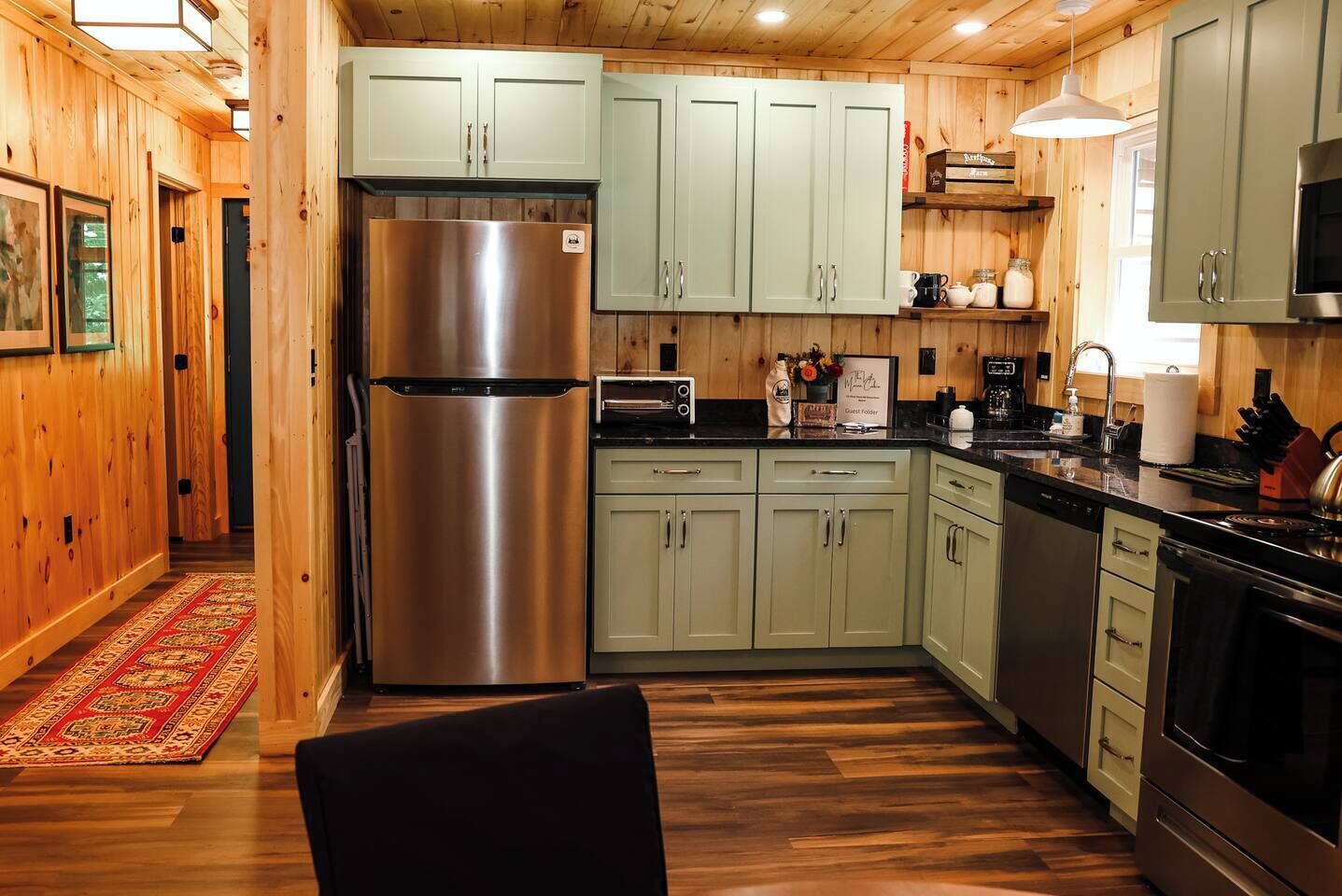 A modern kitchen with wooden walls, a stainless steel refrigerator, a microwave, and a sink.