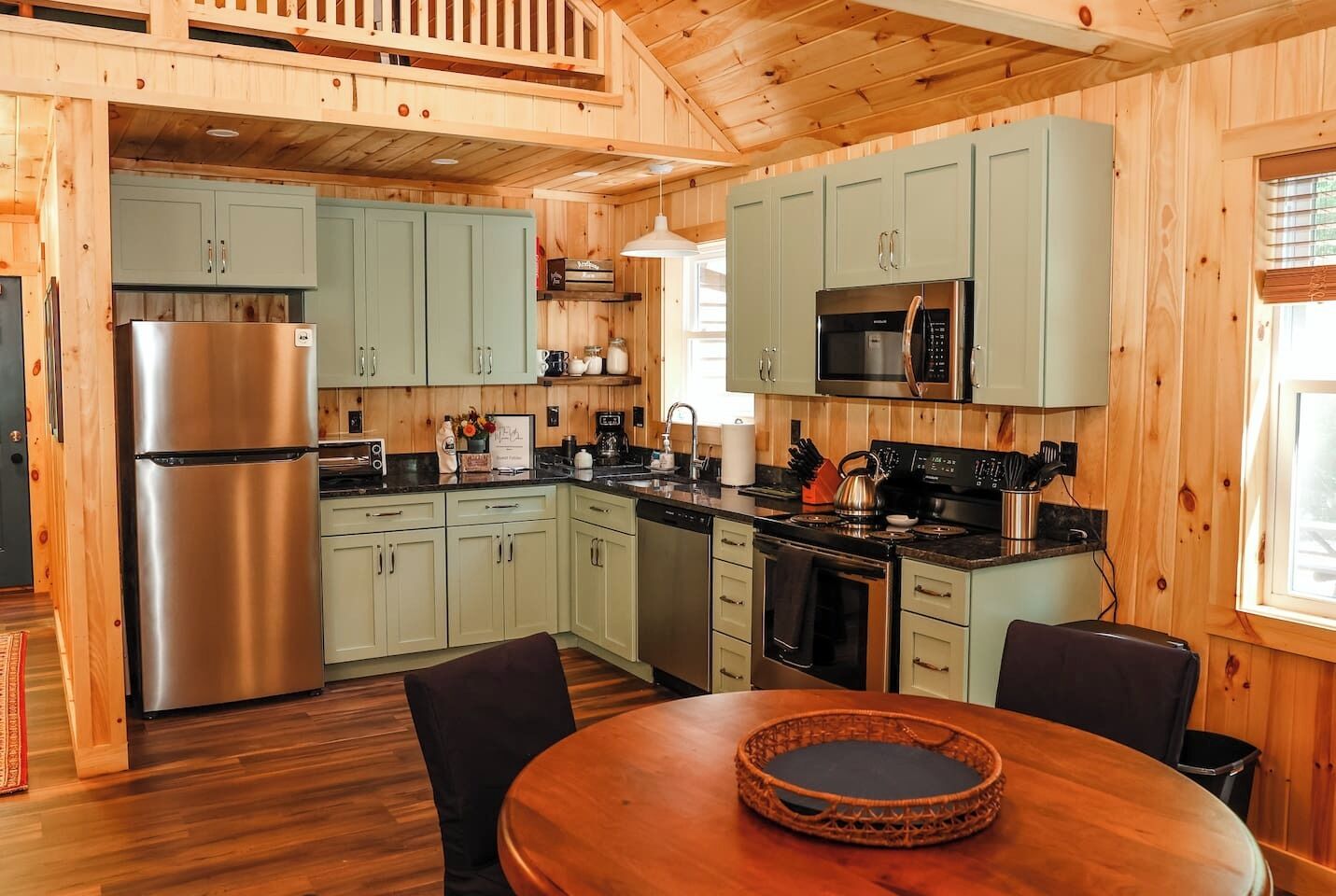 A wooden cabin-style kitchen with a stainless steel refrigerator, light green cabinets, a microwave, and a stove.