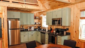 Eine holzgetäfelte Küchenzeile mit Edelstahl-Kühlschrank, hellgrünen Schränken, einer Mikrowelle und einem Herd.