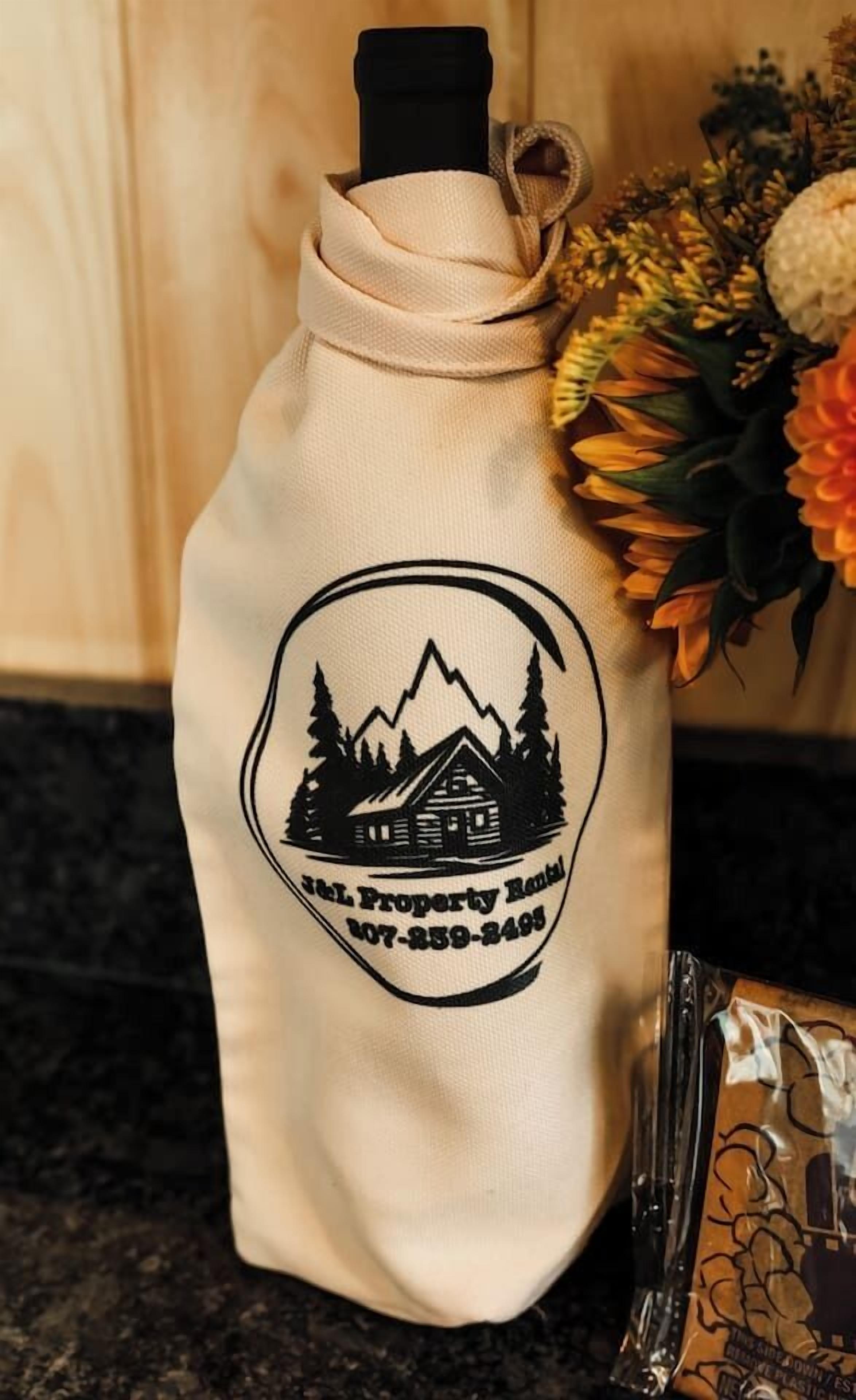 A beige tote bag with a cabin and mountains graphic, and a phone attached to the top.
