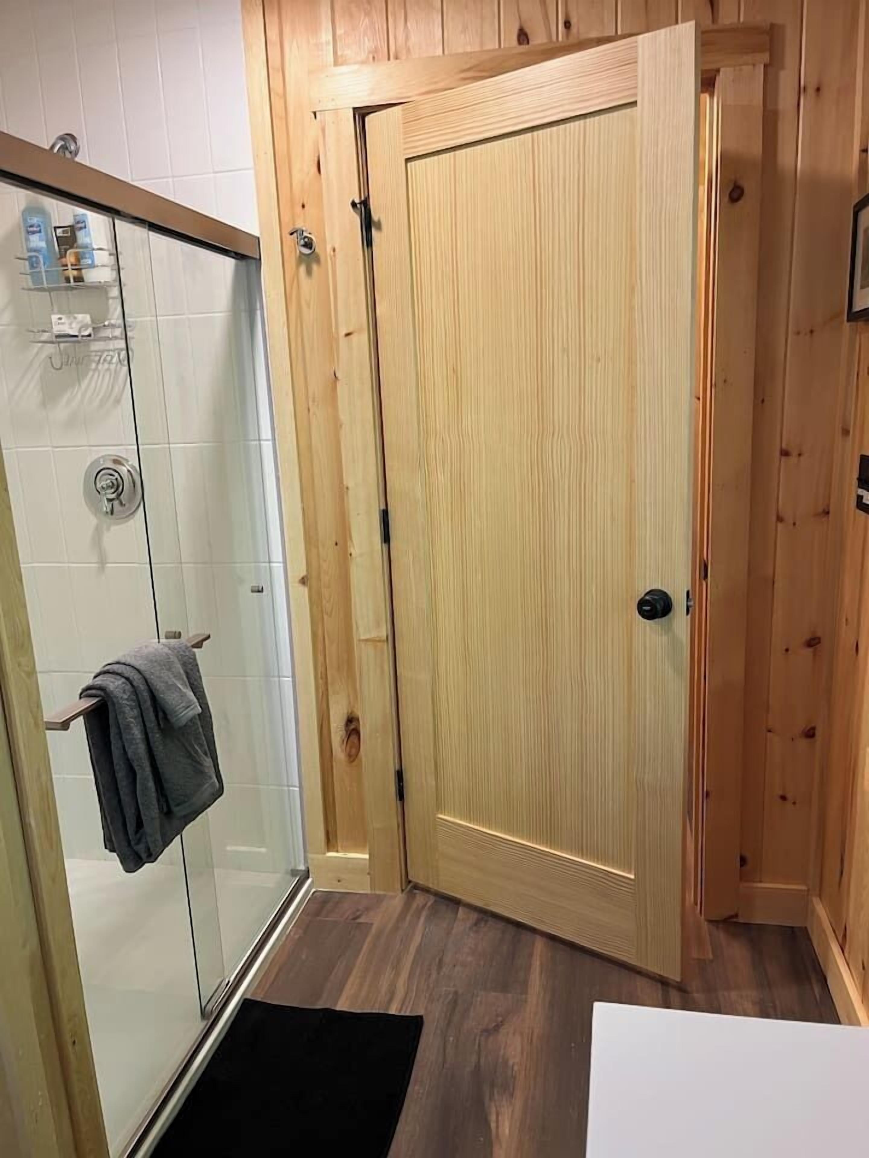 A bathroom with a glass shower enclosure, a wooden door, and a towel rack with a towel.
