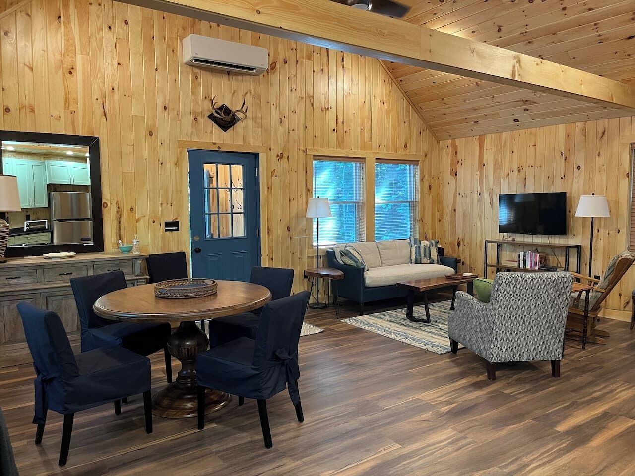 A wooden cabin interior with a dining area, sofa, TV, and kitchen.