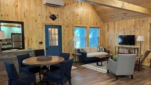 Ein Holzblockhaus-Interieur mit Essbereich, Sofa, Fernseher und Küche.
