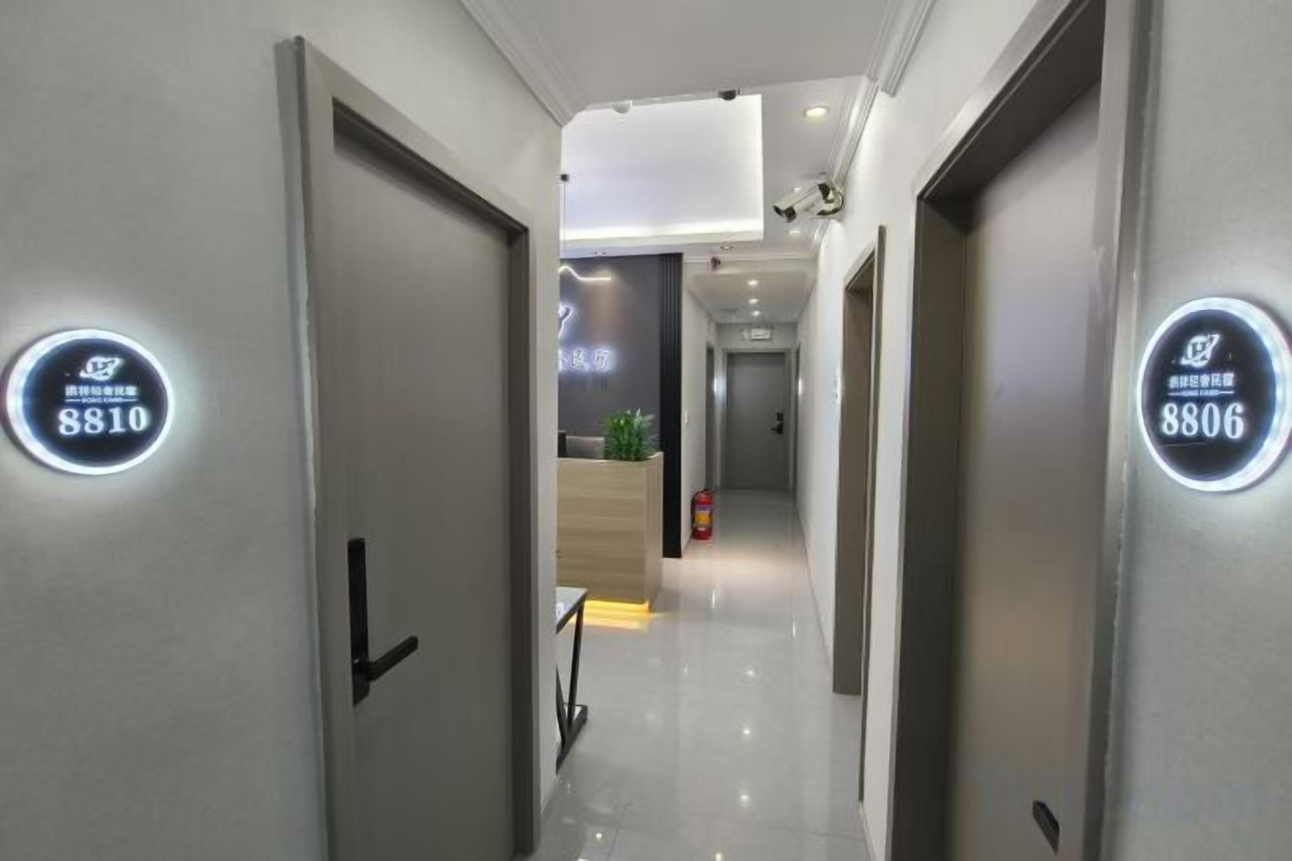 A hotel corridor with doors labeled 8810 and 8806, leading to a reception area with a plant and a fire extinguisher.