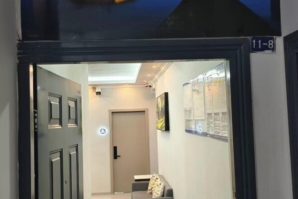 A hallway with a closed door, a small seating area with a cushion, and a wall-mounted information board. - Tianshun Apartment (Chongqing)