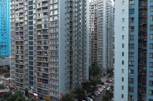 Um edifício residencial alto com vários andares, varandas e uma área de estacionamento na frente.