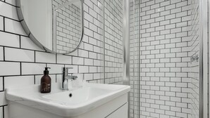 Un baño con un lavabo blanco, un espejo y una zona de ducha con azulejos blancos.