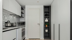 Una cocina compacta con armarios blancos, piso con patrón de espiga y una puerta que da a una despensa.