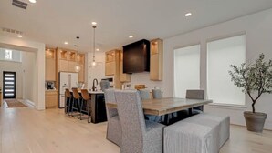 A modern kitchen with a dining area, wooden cabinets, a large island, and a potted plant. - Modern 4BR Retreat, BBQ & Dining in The Woodlands (Tomball)