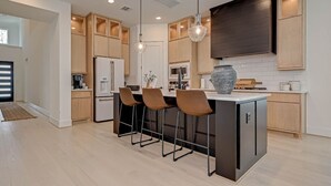 A modern kitchen with wooden cabinets, a central island with bar stools, pendant lighting, and a large vase. - Modern 4BR Retreat, BBQ & Dining in The Woodlands (Tomball)