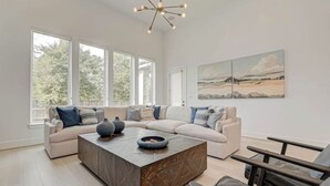 A spacious living room with a large sectional sofa, a coffee table, and a modern chandelier. - Modern 4BR Retreat, BBQ & Dining in The Woodlands (Tomball)