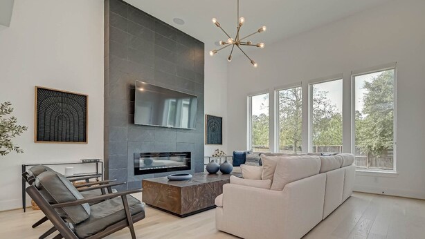A modern living room with a large flat-screen TV, a fireplace, a sofa, and a coffee table. - Modern 4BR Retreat, BBQ & Dining in The Woodlands (Tomball)