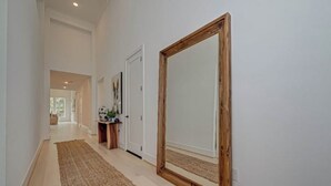A hallway with a wooden-framed mirror, a rug, and a door leading to another room. - Modern 4BR Retreat, BBQ & Dining in The Woodlands (Tomball)