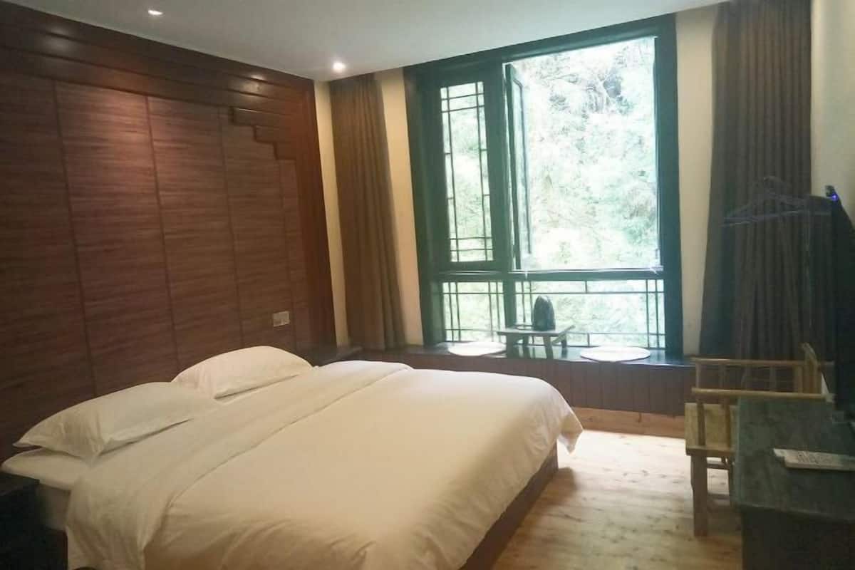 A bedroom with a large bed, a small table, and a window with a view of trees.