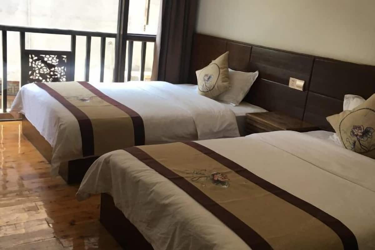Two beds with matching headboards and decorative pillows, a wooden floor, and a balcony with a patterned screen.