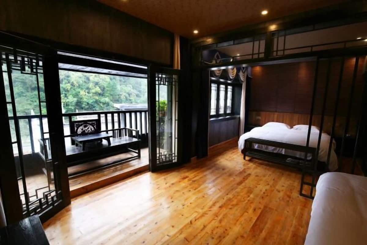 A room with wooden flooring, a bed, a table, and a view through a window.