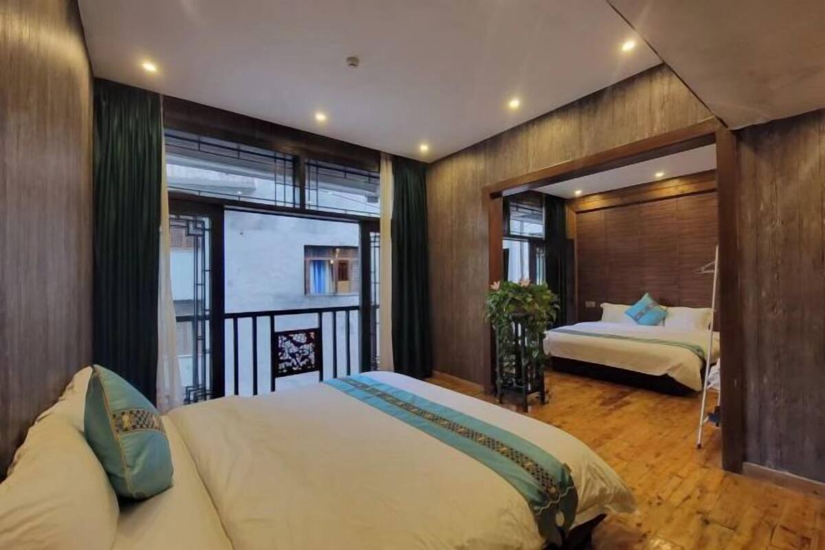 A hotel room with a large bed, a smaller bed, a balcony, and a view of the cityscape.