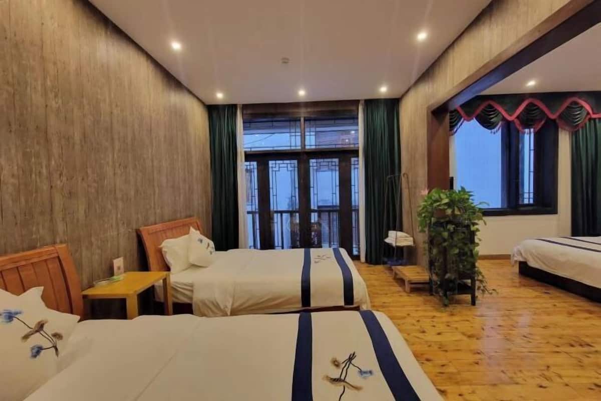 A hotel room with two beds, wooden flooring, a large window with curtains, and a plant.