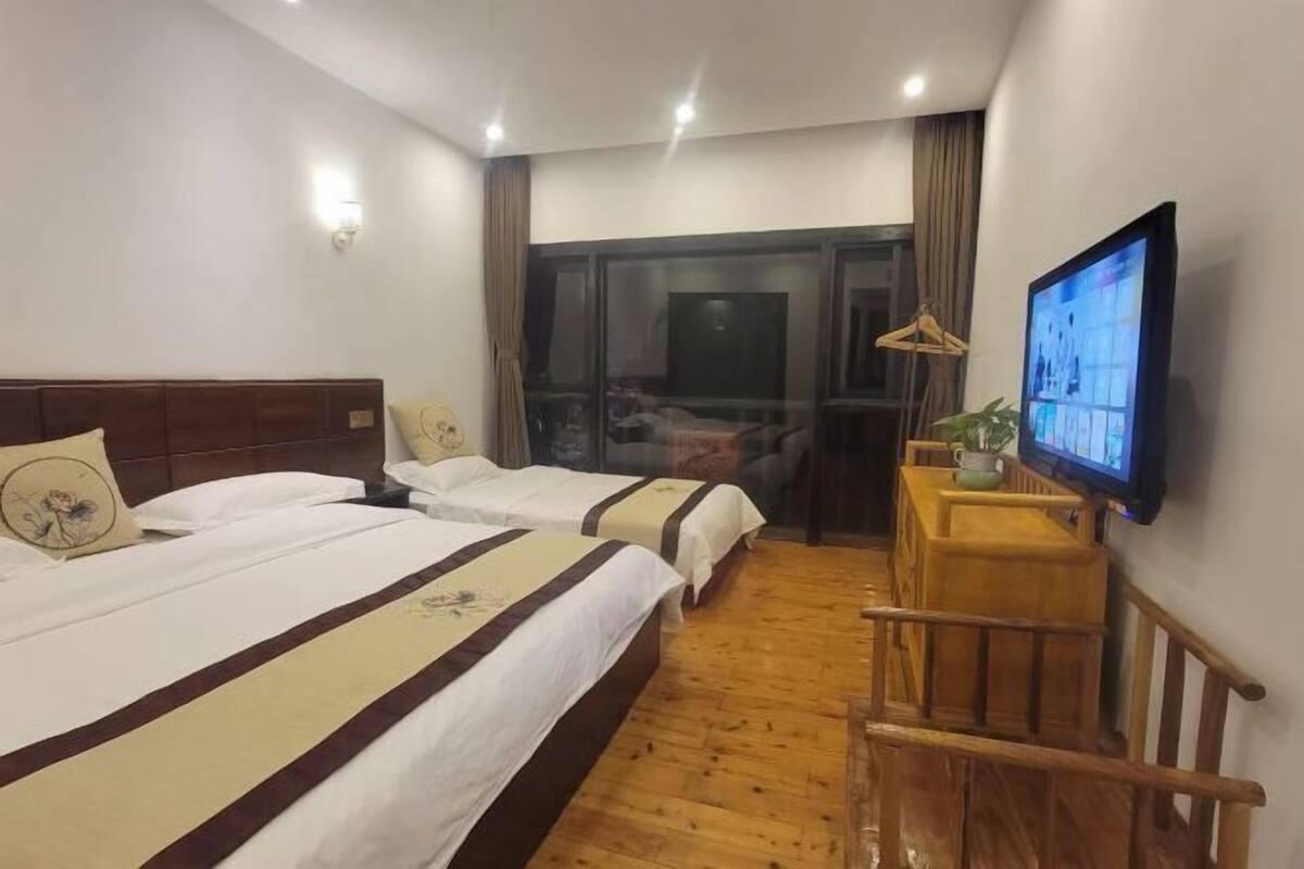 A hotel room with two beds, a TV, a wooden desk, and a window with curtains.