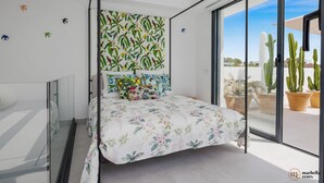 A modern bedroom with a bed, a TV, and a view of cacti through a sliding glass door.