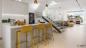 A modern kitchen with a central island, bar stools, and a staircase leading to a living area with a view.
