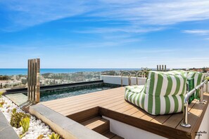 A rooftop pool with a wooden deck, green-striped cushions, and a clear view of the sea and cityscape. - Penthouse Casa Volver | Ref. #74 (Marbella)