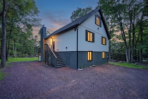 Ein zweigeschossiges Haus mit einer Treppe, die zum Eingang führt, umgeben von einem Schotterweg und Bäumen.