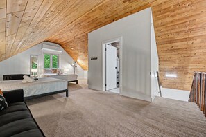 A bedroom with a sloped ceiling, a bed, a nightstand, and a window with a view of trees.