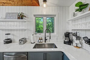 A kitchen with white cabinetry, a blender, a toaster, a coffee maker, and a window with a view of trees.