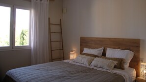 A bedroom with a wooden headboard, a bed with white bedding, a nightstand with a lamp, a ladder against the wall, and a window with white curtains. - Casa Looma Splash in the lovely swimming pool (Benitachell)