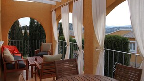 A balcony with wooden furniture, white curtains, and a view of the cityscape. - Casa Looma Splash in the lovely swimming pool (Benitachell)