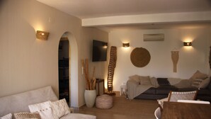 A living room with a sofa, a wooden dining table, and a TV mounted on the wall. - Casa Looma Splash in the lovely swimming pool (Benitachell)