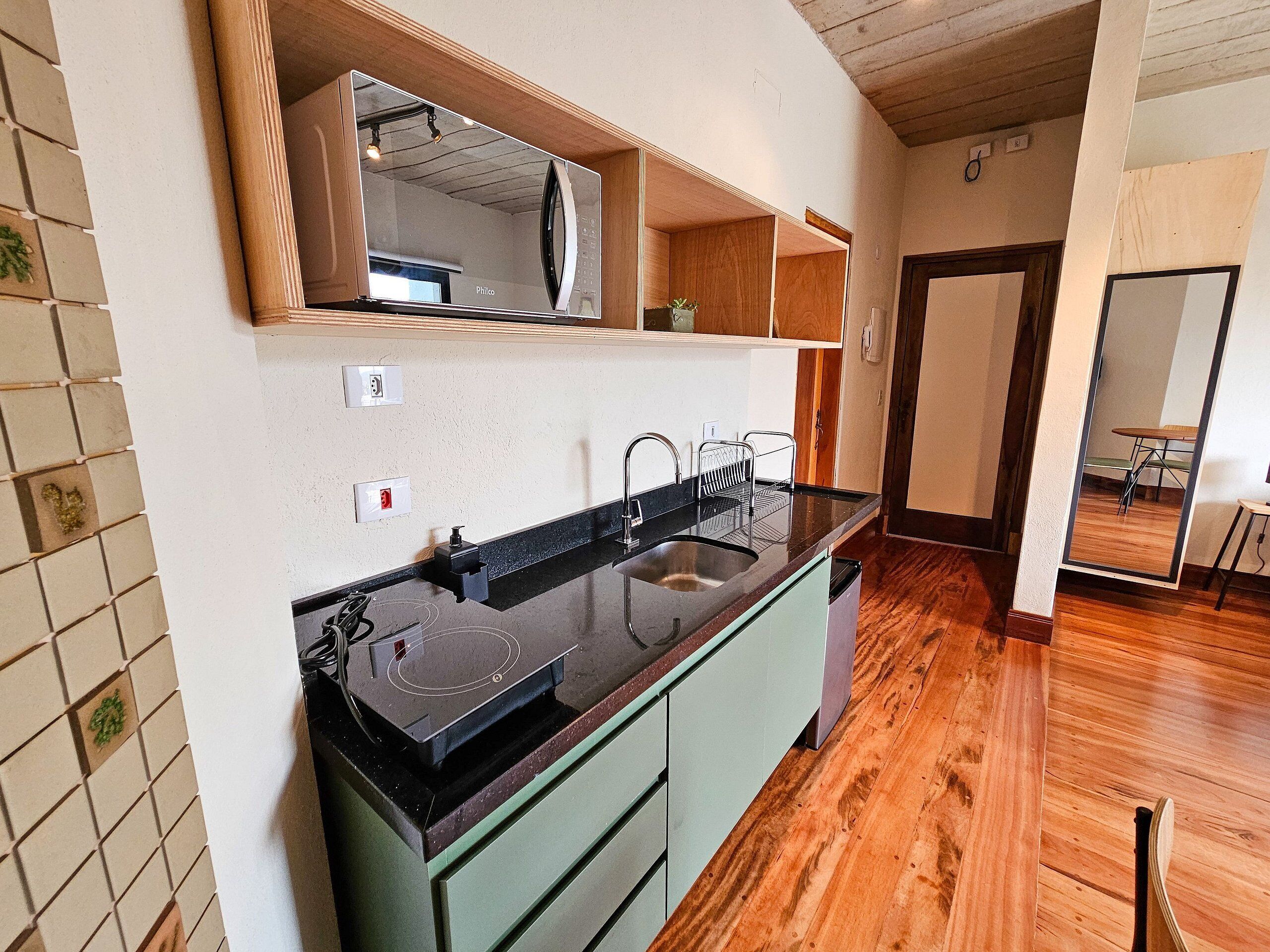 A kitchen with a black countertop, a sink, and a built-in microwave. There are wooden cabinets and a mirror above the counter.