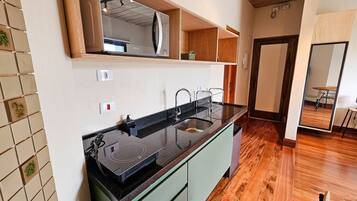 A kitchen with a black countertop, a sink, and a built-in microwave. There are wooden cabinets and a mirror above the counter.