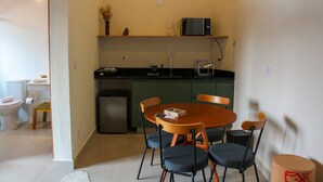 A compact kitchen with a microwave, sink, and a small refrigerator. There is a dining table with four chairs and a vase with dried flowers on the counter. - Estudios no Capivari by The Lodges (Campos do Jordão)