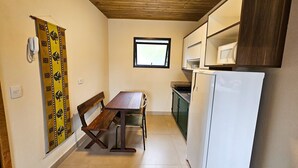 A compact kitchen with a wooden ceiling, a dining table with a bench, a white refrigerator, and a window.