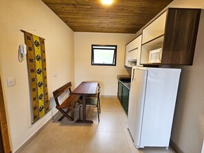 A compact kitchen with a wooden ceiling, a dining table with a bench, a white refrigerator, and a window.