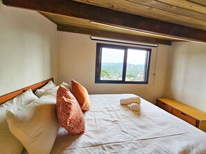 Une chambre à coucher avec un lit, des oreillers, une fenêtre et un banc en bois.