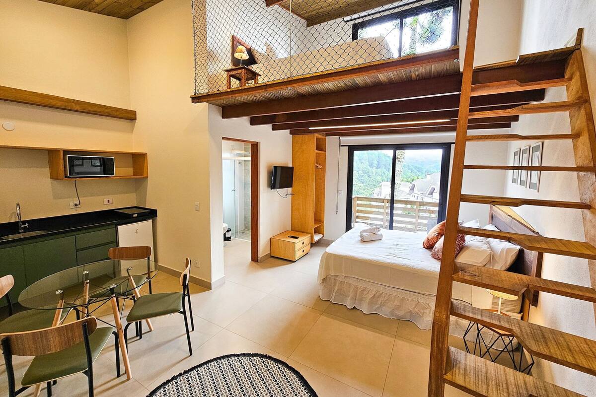 A compact hotel room with a loft bed, a small bathroom, and a dining area with chairs and a table.