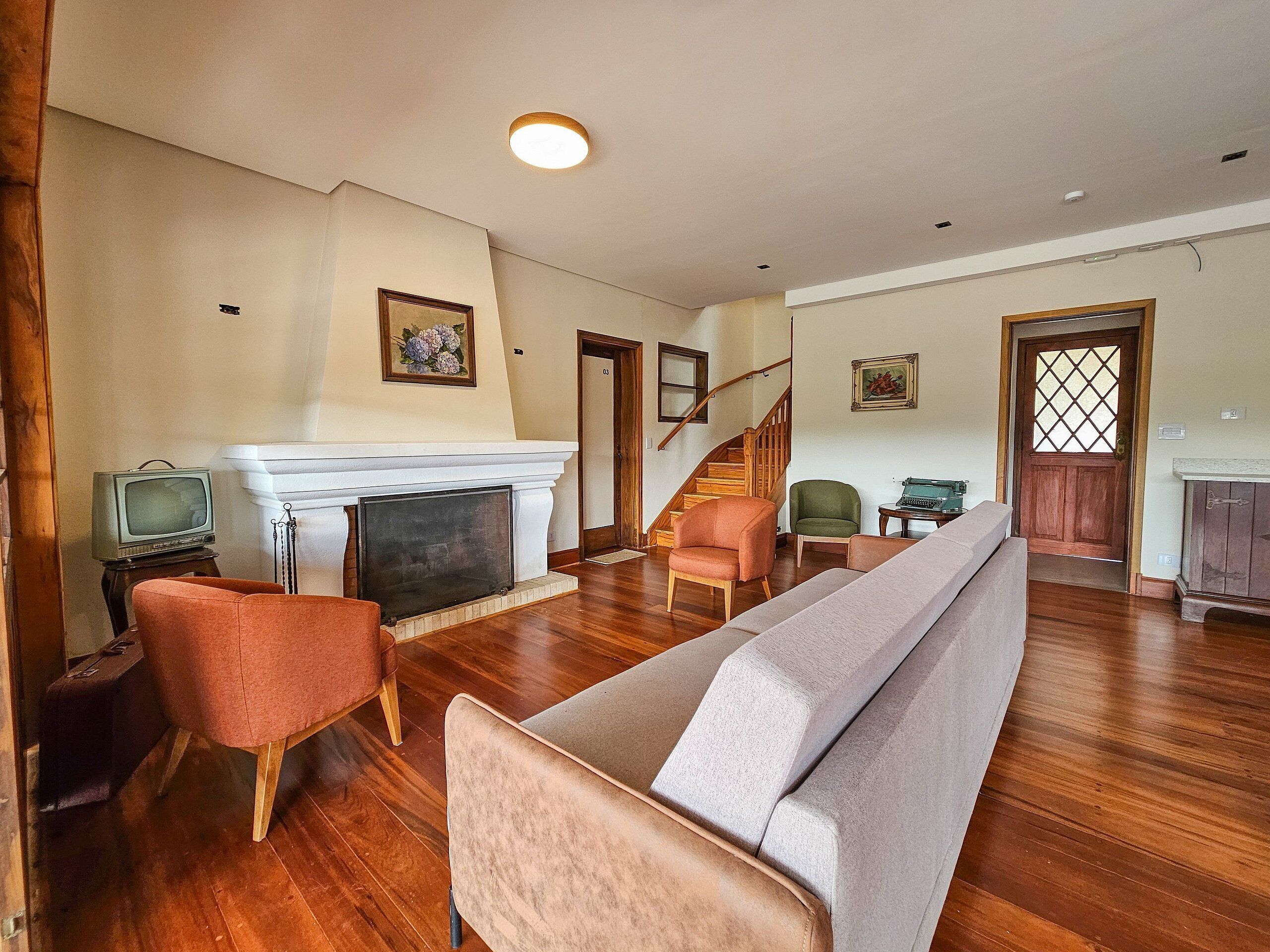 A spacious living room with a fireplace, wooden flooring, and a staircase leading to another level.
