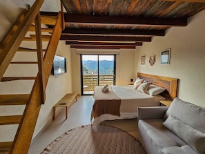 Ein Schlafzimmer mit einer Holztreppe, einem Bett mit Kissen, einer Couch und einem Fernseher an der Wand.