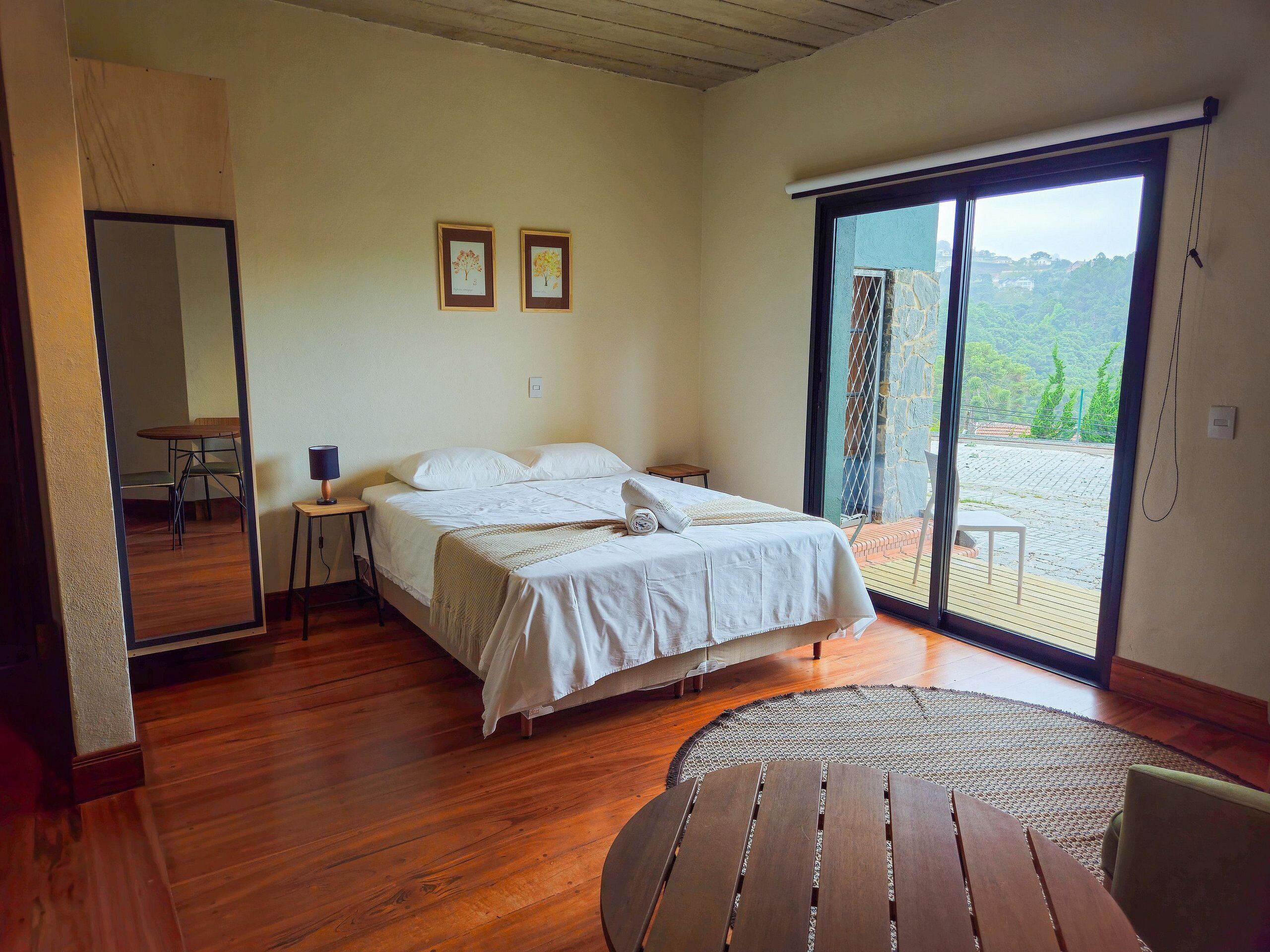 Quarto com cama, mesa e vista pela porta deslizante.