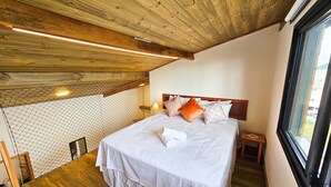 A bedroom with a wooden ceiling, a bed with white bedding, and a view through a window. - Estudios no Capivari by The Lodges (Campos do Jordão)