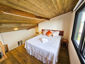 Ein Schlafzimmer mit Holzboden, einem Bett mit weißer Bettwäsche und Blick durch ein Fenster.