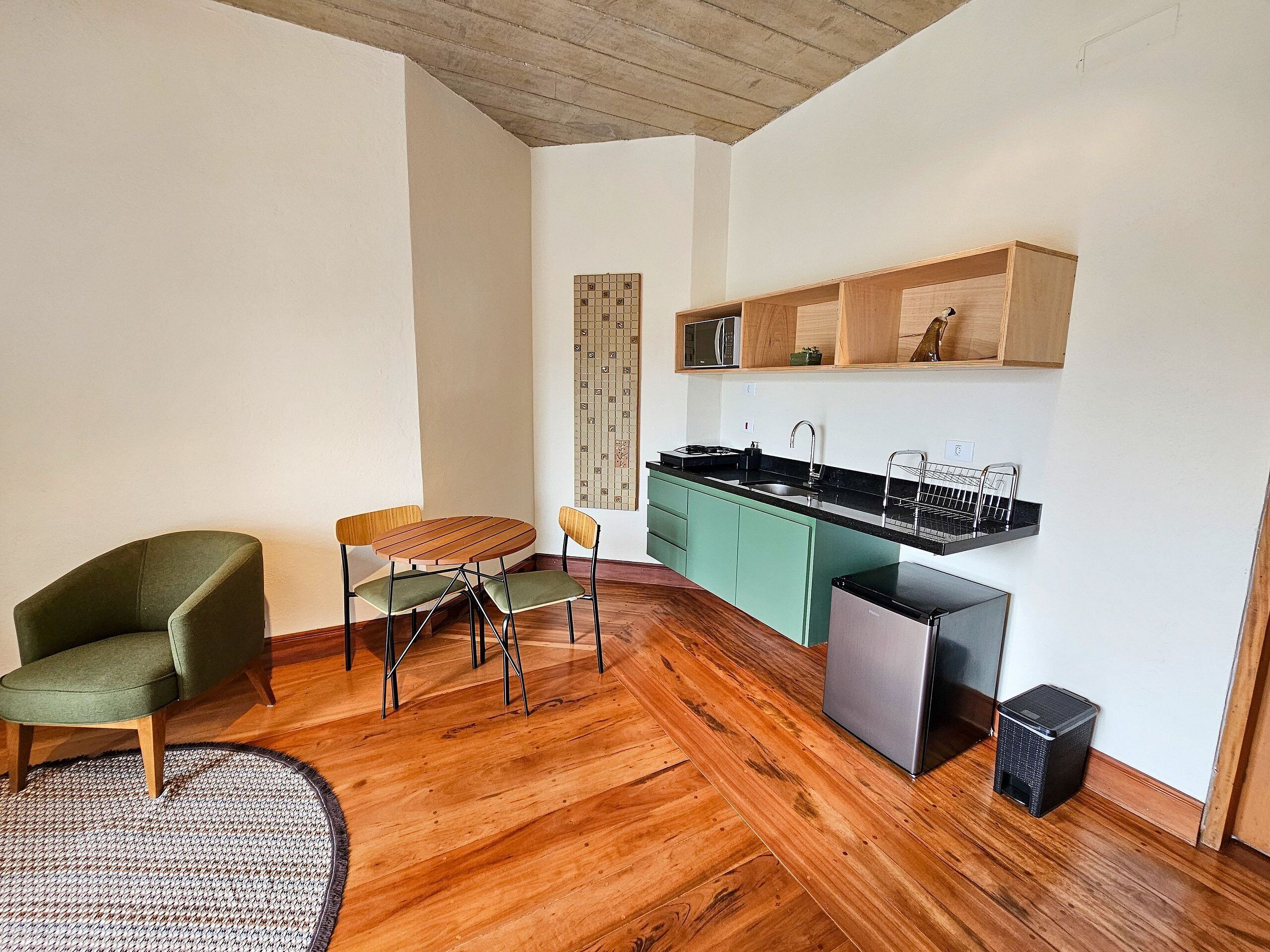 A compact living space with a wooden floor, a dining table with chairs, a kitchen area with a sink and cabinets, and a small trash bin.