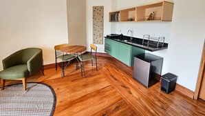 A compact living space with a wooden floor, a dining table with chairs, a kitchen area with a sink and cabinets, and a small trash bin. - Estudios no Capivari by The Lodges (Campos do Jordão)