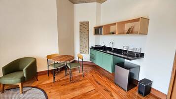 A compact living space with a wooden floor, a dining table with chairs, a kitchen area with a sink and cabinets, and a small trash bin.